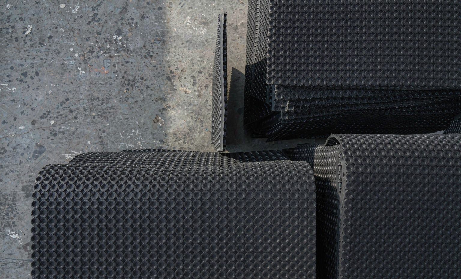 Black rubber livestock mats with coin-groove surface stacked on a factory floor